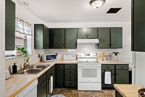 A compact kitchen with dark cabinets, a microwave, an oven, and a sink. - Casa de Knight 2.0 (Las Cruces)