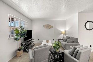 Uma sala de estar moderna com sofás cinzas, uma mesa de centro, uma televisão e uma luminária.