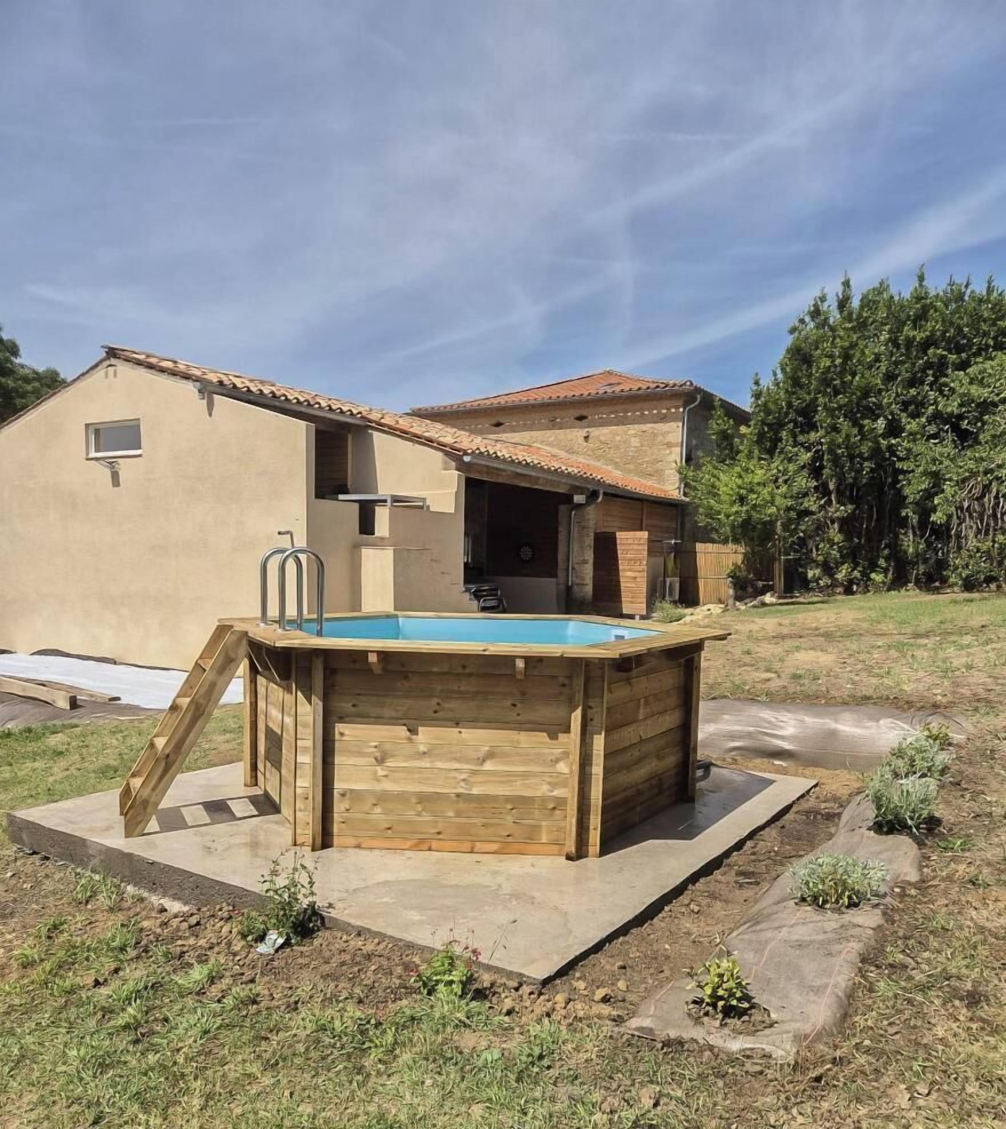 A wooden hot tub with a ladder, a house with a tiled roof, and a grassy yard.