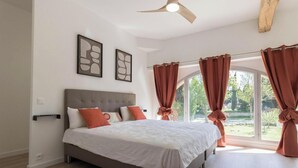 A bedroom with a bed, curtains, a ceiling fan, and artwork. - Pareine - BEAUTEVILLE (BEAUTEVILLE)