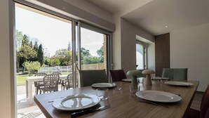 A dining area with a wooden table set for four, large windows, and a view of a garden. - Pareine - BEAUTEVILLE (BEAUTEVILLE)
