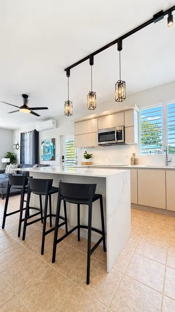 A modern kitchen with a central island, bar stools, pendant lighting, and a ceiling fan.