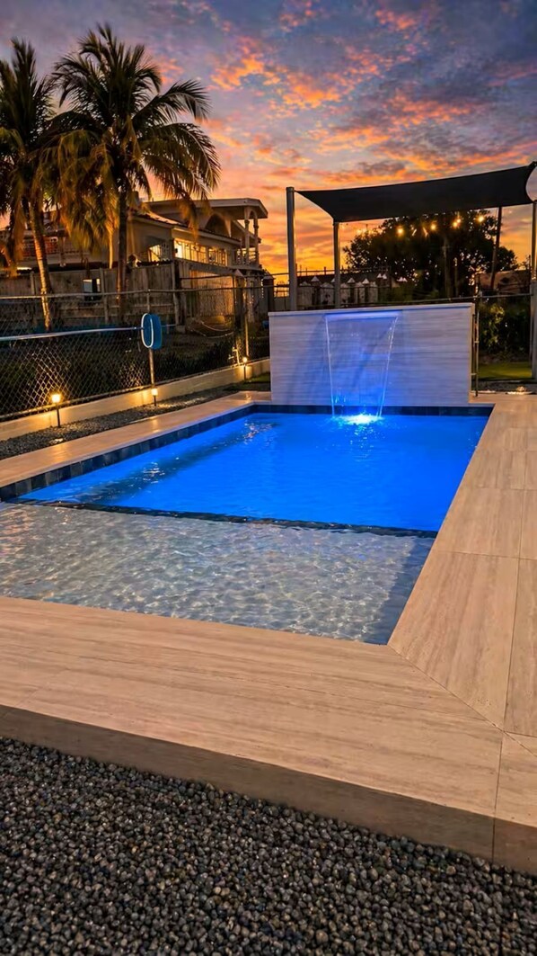 A swimming pool with a water feature, surrounded by a wooden deck and a fence.