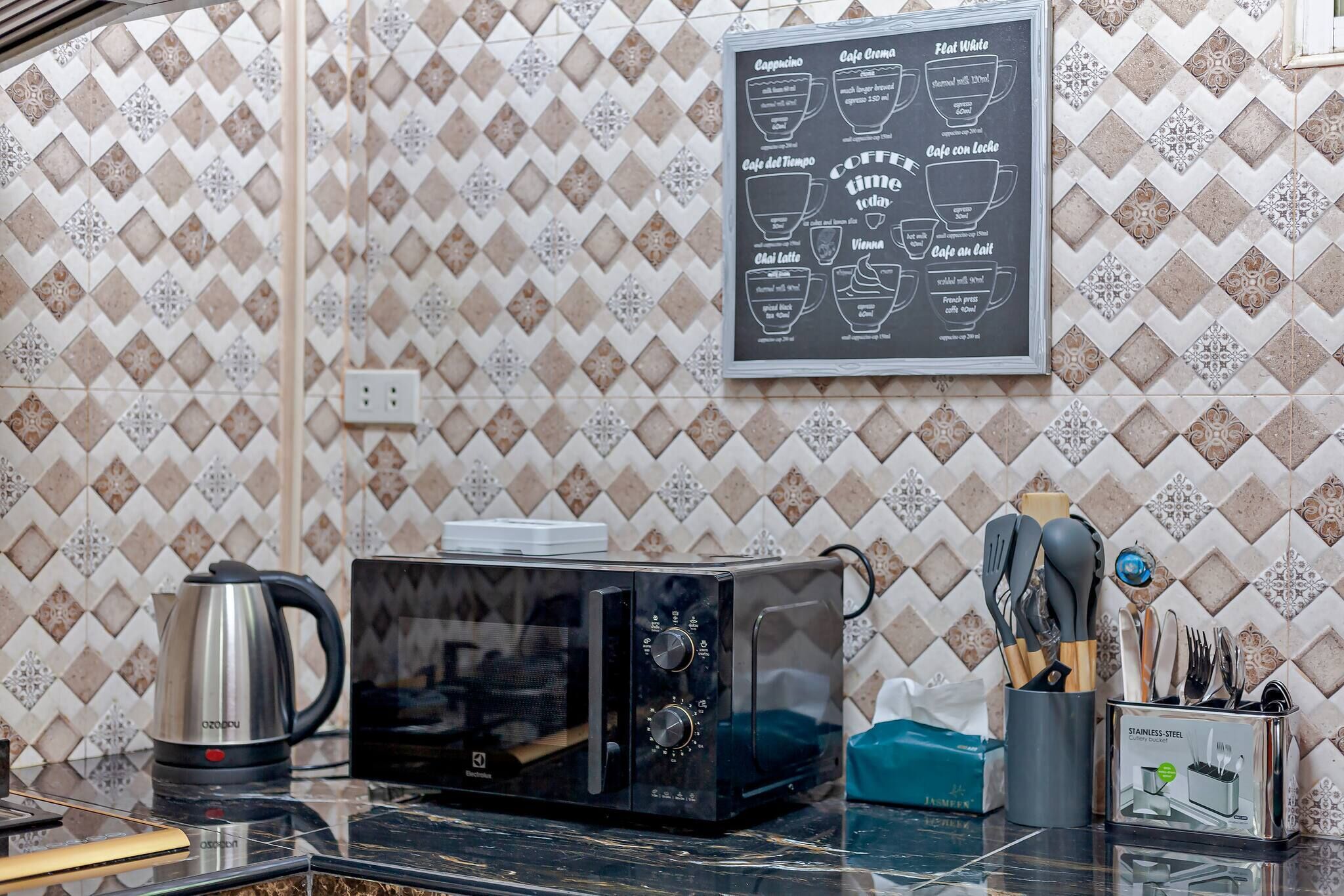 A kitchen with a microwave, kettle, and utensils on the counter.