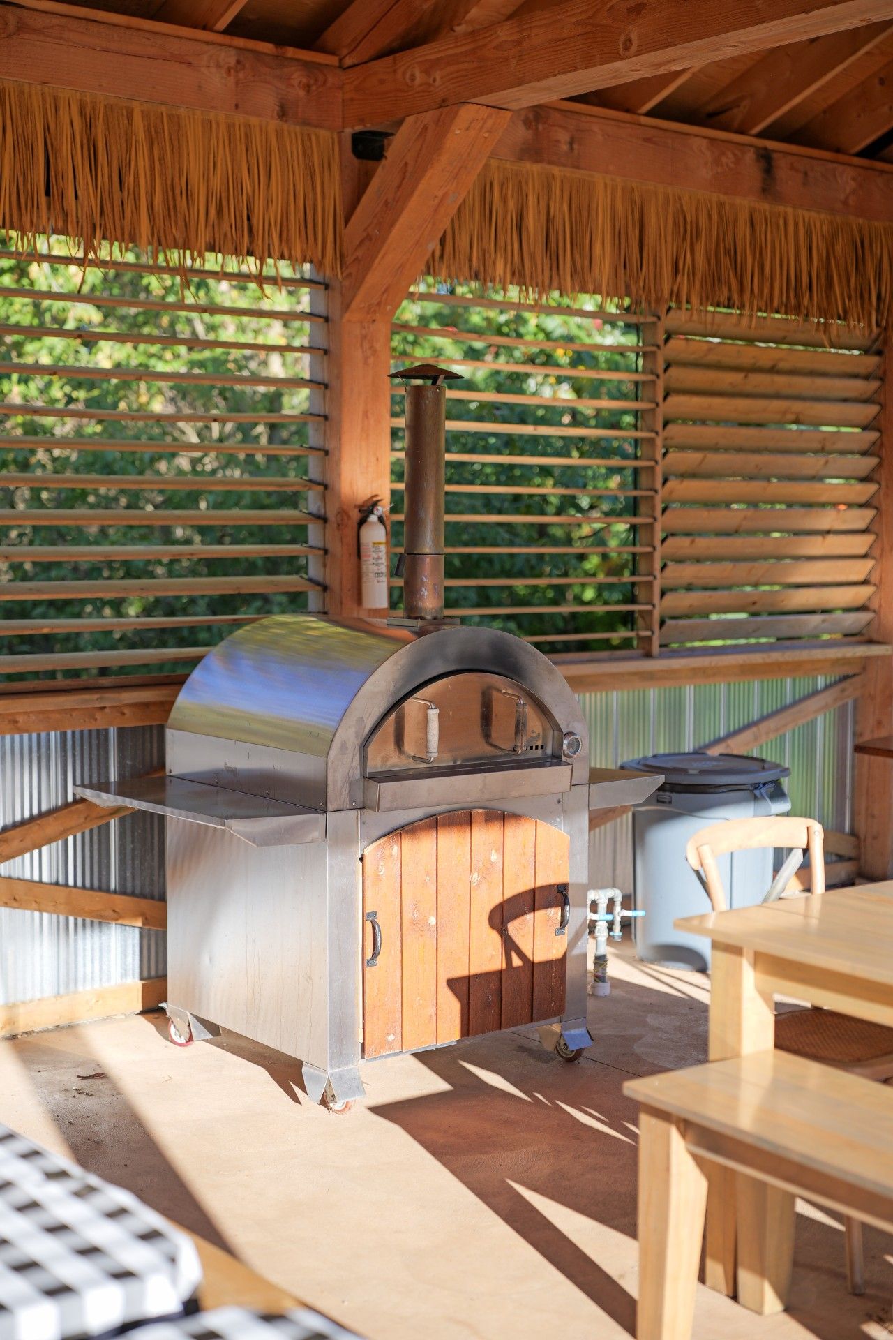 An outdoor patio with a built-in barbecue grill, wooden tables, and a covered seating area.