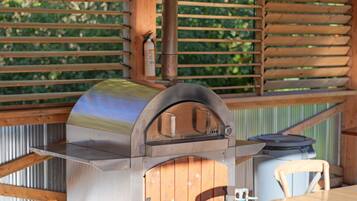 An outdoor patio with a built-in barbecue grill, wooden tables, and a covered seating area.