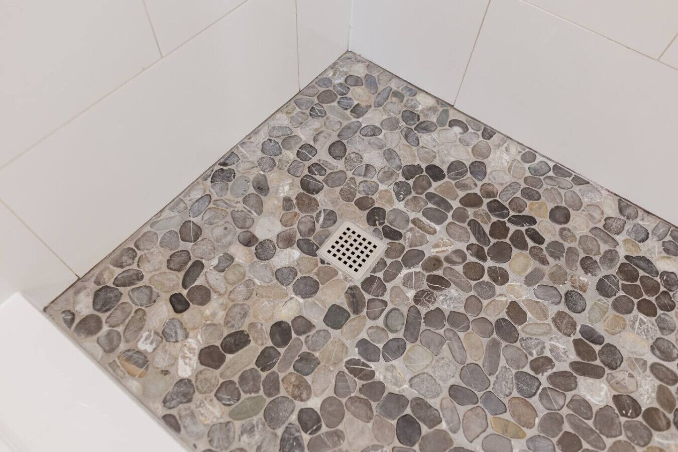 Une douche dont le sol est recouvert de petits galets et dont le drain est situé au centre.