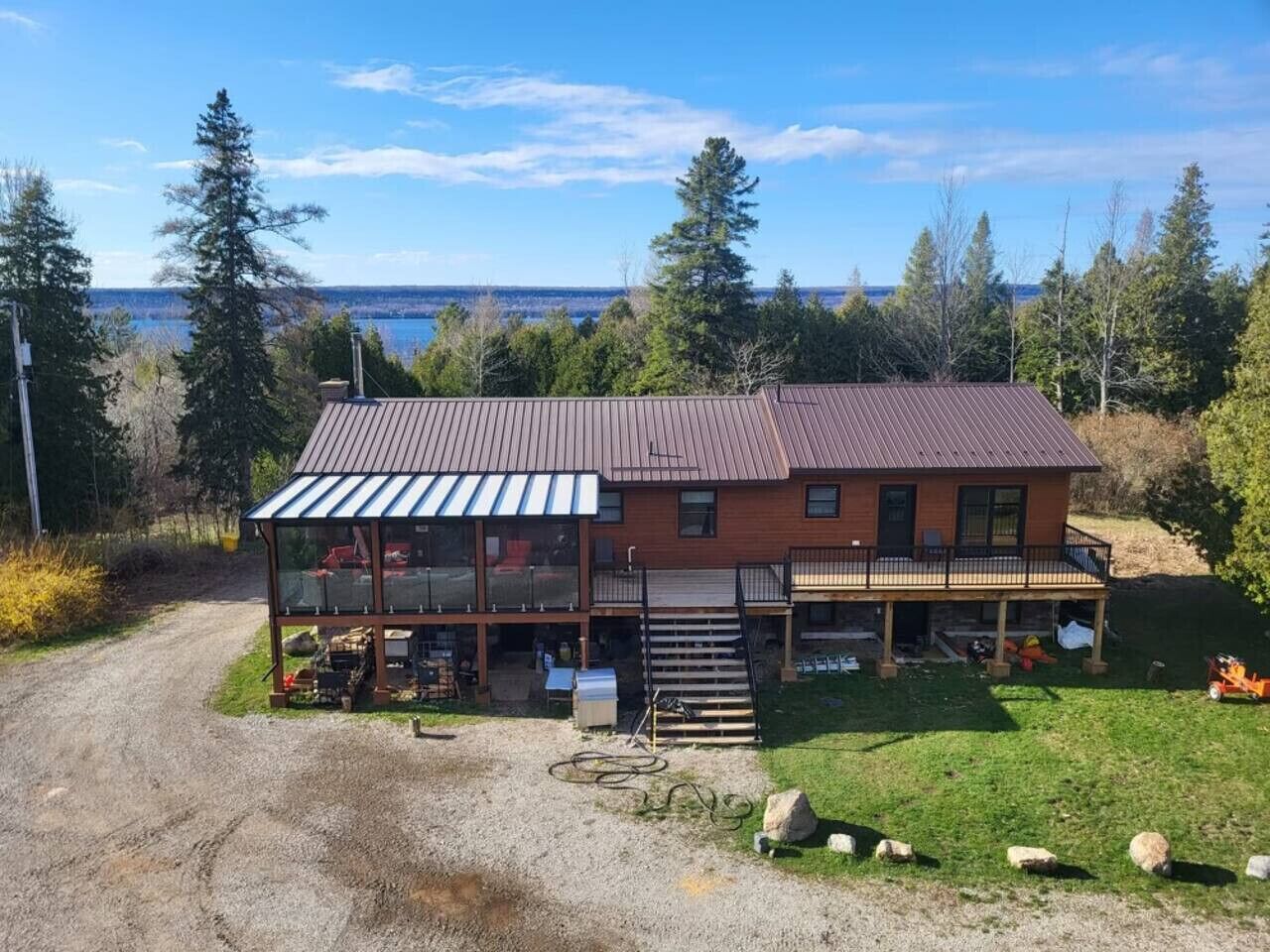 A two-story wooden house with a balcony, a covered porch, and a view of a lake.