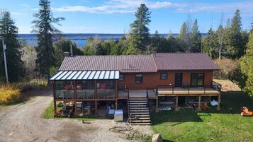 A two-story wooden house with a balcony, a covered porch, and a view of a lake.