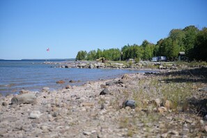 A rocky shoreline with a body of water, trees, and a small structure.