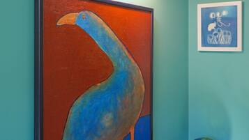 Una pared color turquesa con un cuadro enmarcado de un pájaro, un accesorio de luz fijado a la pared y un pequeño globo terráqueo sobre un soporte.