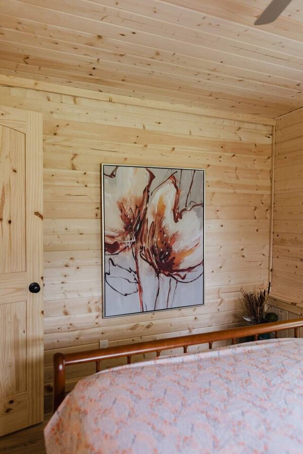 A wooden room with a bed, a wooden door, and a wall-mounted painting.
