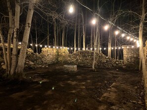 Un muro de piedra, árboles y una zona pavimentada de noche.