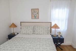 Una camera da letto con un letto, due comodini, una lampada, un quadro appeso al muro e una finestra con tende.