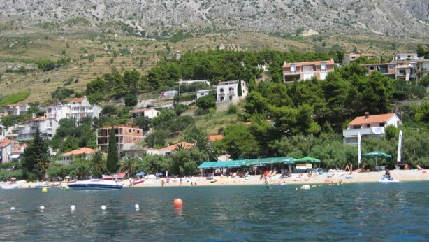 A coastal town with buildings on a hillside, a beach with umbrellas, and boats in the water. - Seaview Family Apartment With Grand Terrace (Omis)