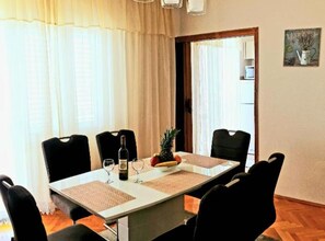 A dining area with a table set for four, chairs, a bottle of wine, and a pineapple. - Seaview Family Apartment With Grand Terrace (Omis)