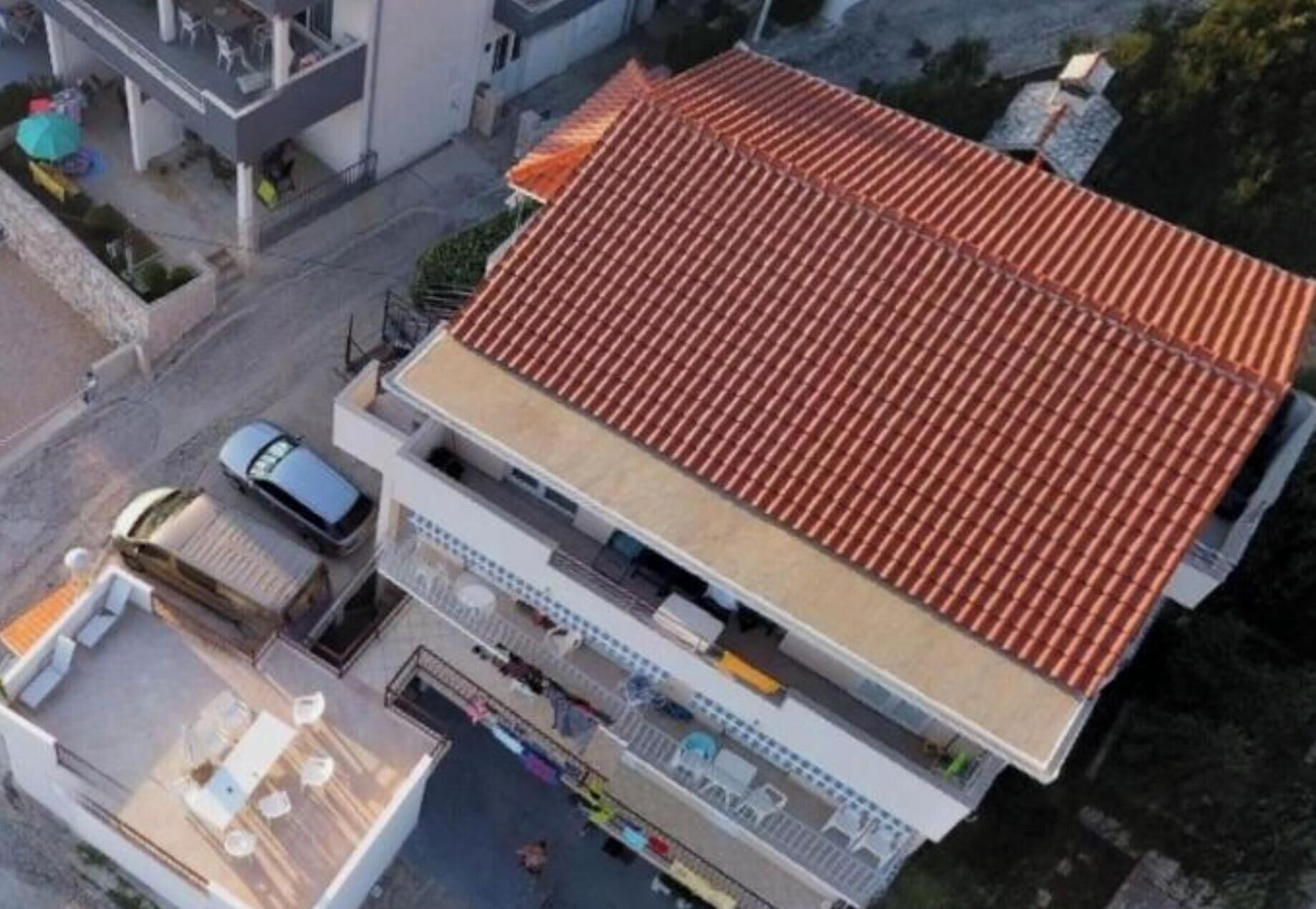 A modern building with a red-tiled roof, a covered outdoor area with seating, and a visible car parked in front.