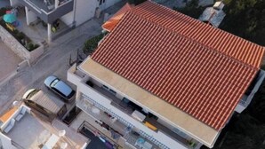 An aerial view of a modern building with a red-tiled roof, a covered outdoor seating area, and a visible car parked in front. - Seaview Family Apartment With Grand Terrace (Omis)