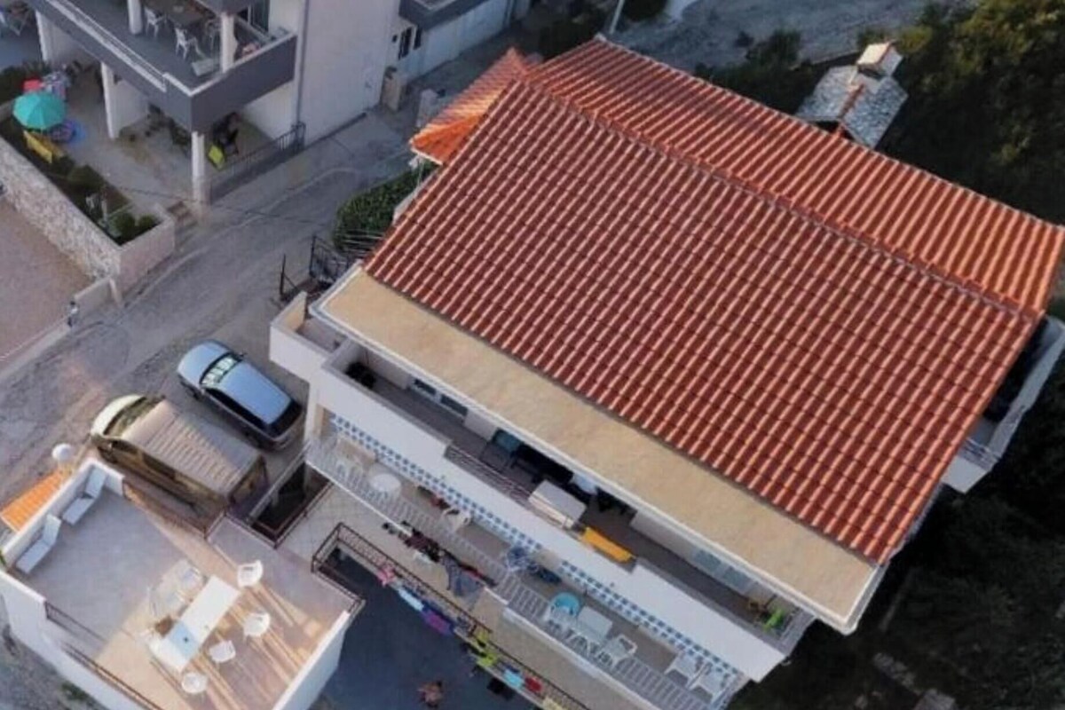 Ein Luftbild eines modernen Gebäudes mit rotem Ziegeldach, einem überdachten Außenbereich und einem sichtbaren Auto vor der Fassade.
