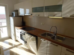 A modern kitchen with white cabinets, a stainless steel sink, a microwave, and a stove. - Seaview Family Apartment With Grand Terrace (Omis)