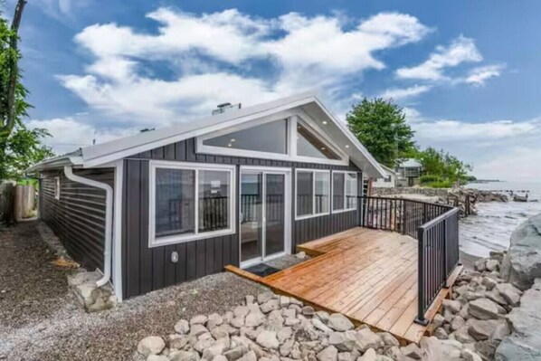 A coastal cabin with a deck, large windows, and a view of the sea.
