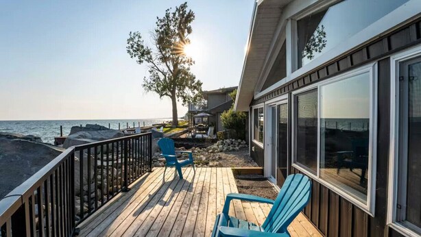 A wooden deck with chairs, a railing, and a view of the ocean.