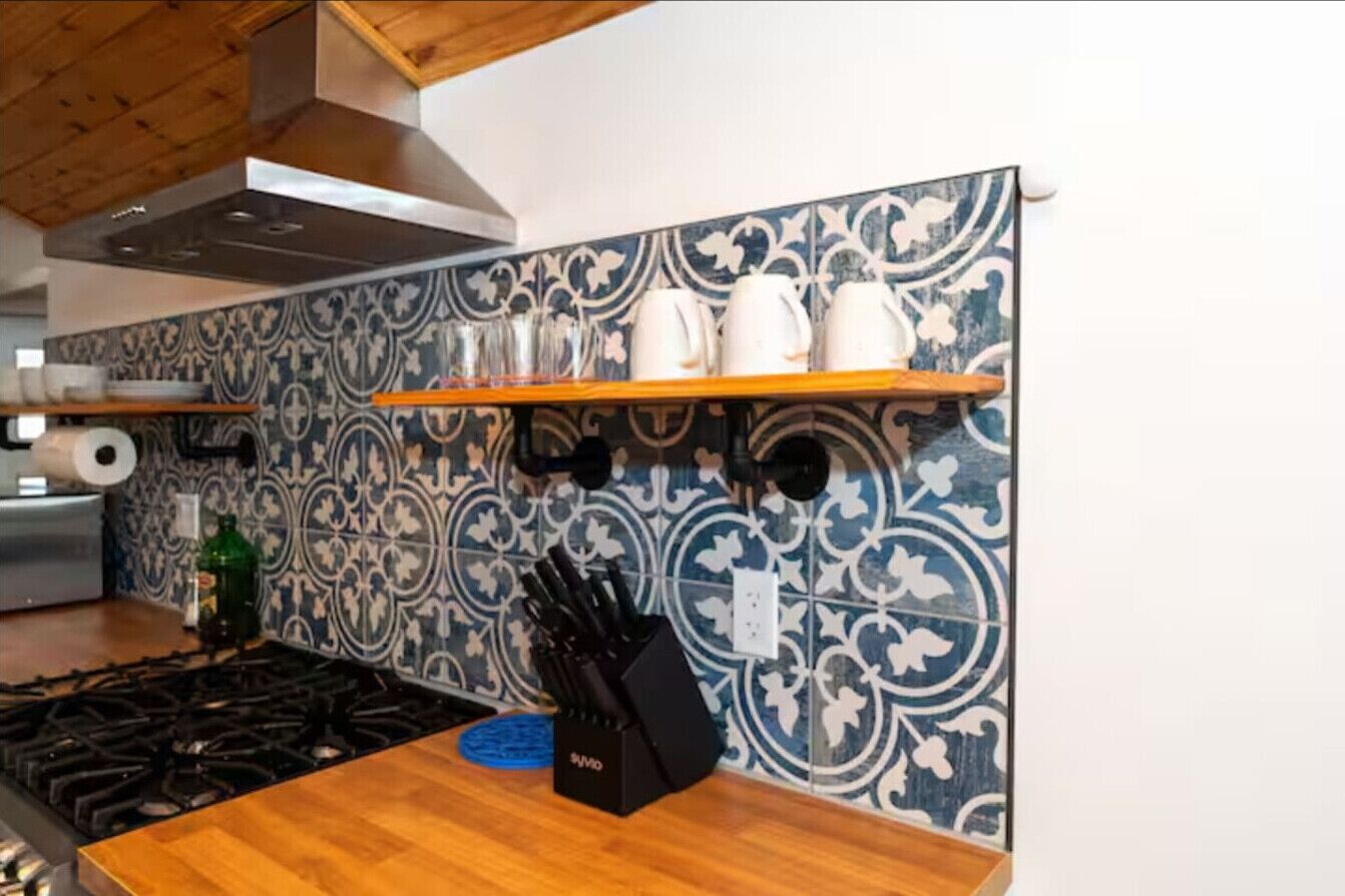 Una cocina con salpicadero estampado, estantes de madera y una estufa a gas.