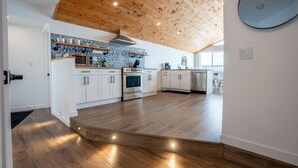 A modern kitchen with white cabinets, stainless steel appliances, and a wooden ceiling.