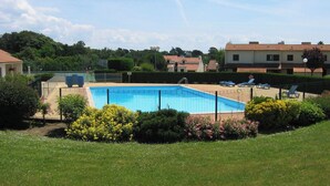 Een zwembad omringd door een hek, met een gazon en struiken op de voorgrond.