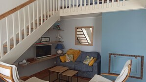 Een woonkamer met een trap, een bank, twee stoelen, een klein tafeltje, een televisie en een spiegel.