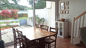 Een eethoek met een houten tafel en stoelen, een kast met glazen deuren en een trap naar een hoger gelegen verdieping.