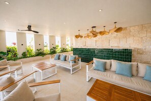 A spacious outdoor lounge area with seating, a stone wall, and hanging lights. - Luxury 2BR | Pool & Golf Views | Juanillo Beach (Punta Cana)