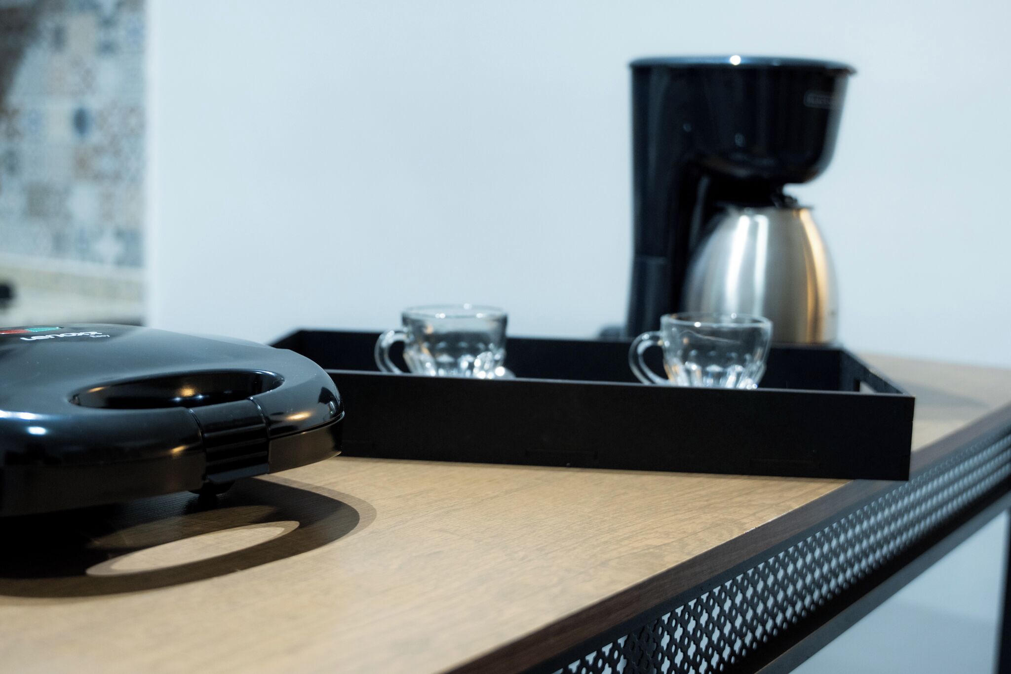 A coffee machine, two glasses, and a tray on a wooden surface.