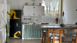 A kitchen with white cabinets, a sink, a window with curtains, a dining table with chairs, and a refrigerator with a cat silhouette. - Room-charming Guest Room With Stunning V (Jardin)