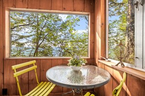 Eine Holzblockhütte mit einem runden Tisch, gelben Stühlen und einem Fenster mit Blick auf Bäume.