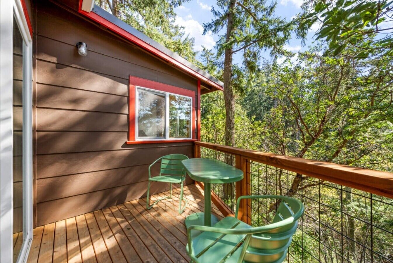 Un terrazzo in legno con tavolo e sedie, una finestra e vista su una foresta.