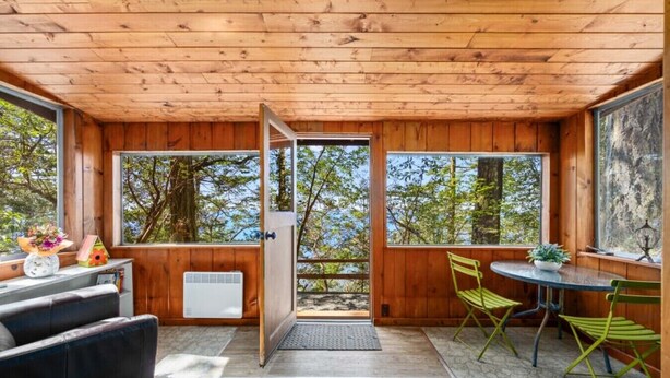Una baita in legno con zona pranzo, divano e vista sugli alberi.