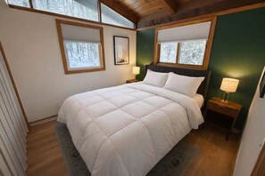 A bedroom with a bed, two bedside tables with lamps, a window with a view of trees, and a green accent wall. - Hot Tub Getaway - Near Killington - Sleeps 12 (Killington)