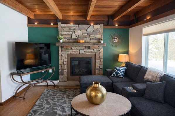 A cozy living room with a stone fireplace, a television, a sofa, and a decorative vase.