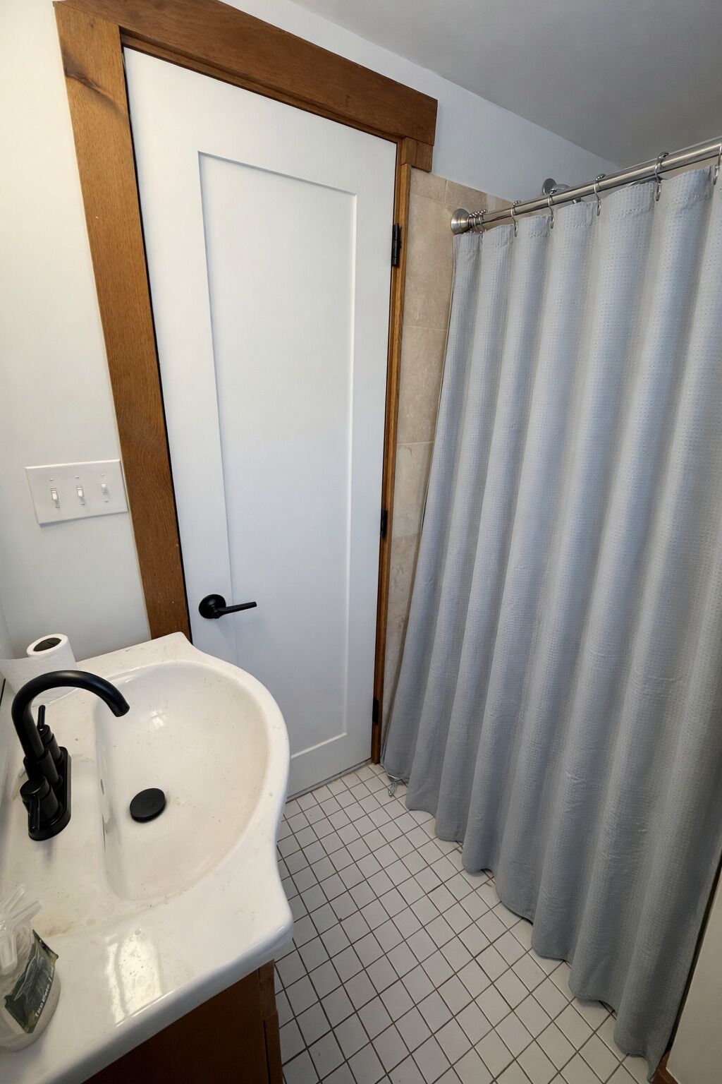 Casa de banho com lavatório branco, uma porta e cortina de chuveiro.