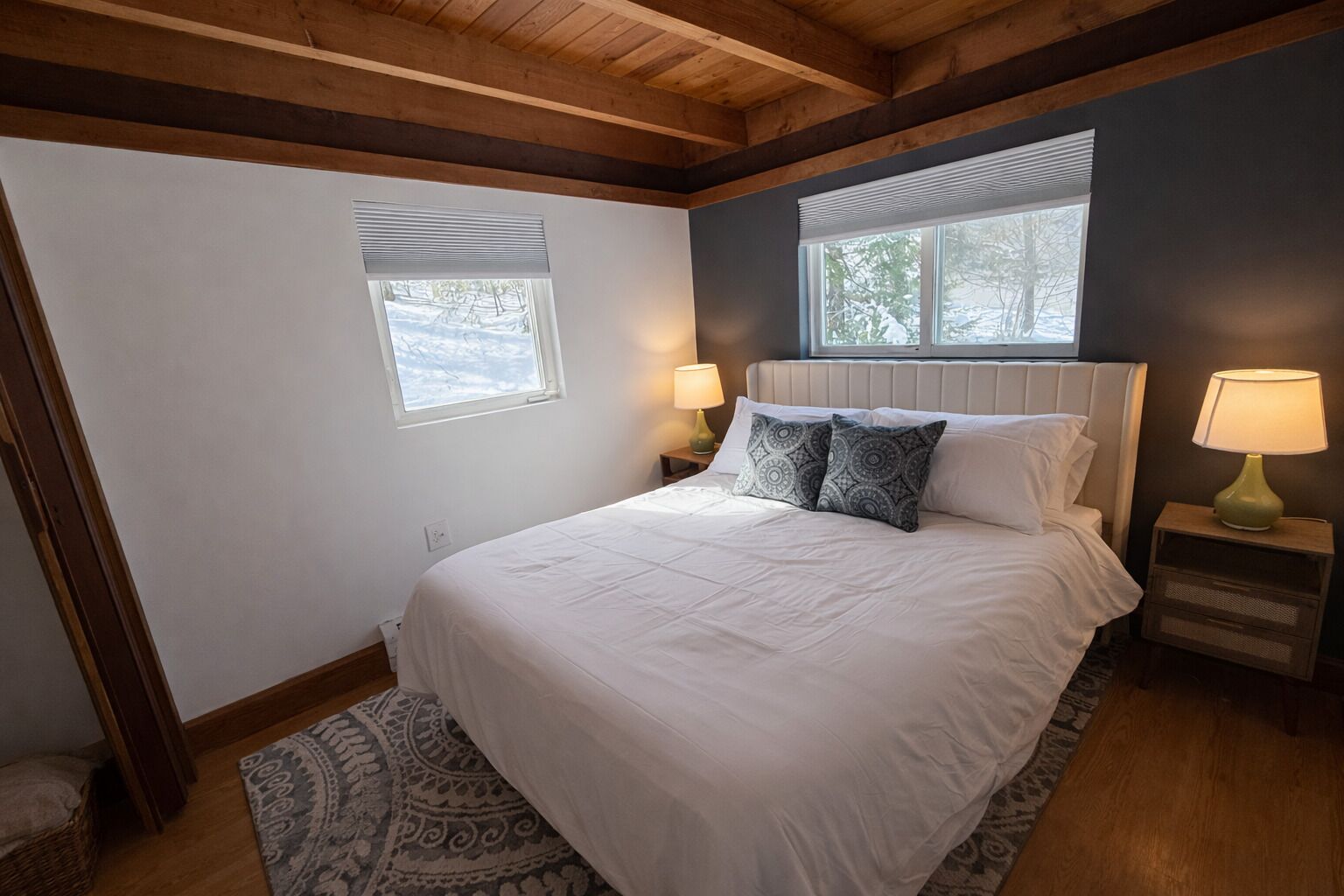 A bedroom with a bed, two bedside tables with lamps, a window, and a patterned rug.