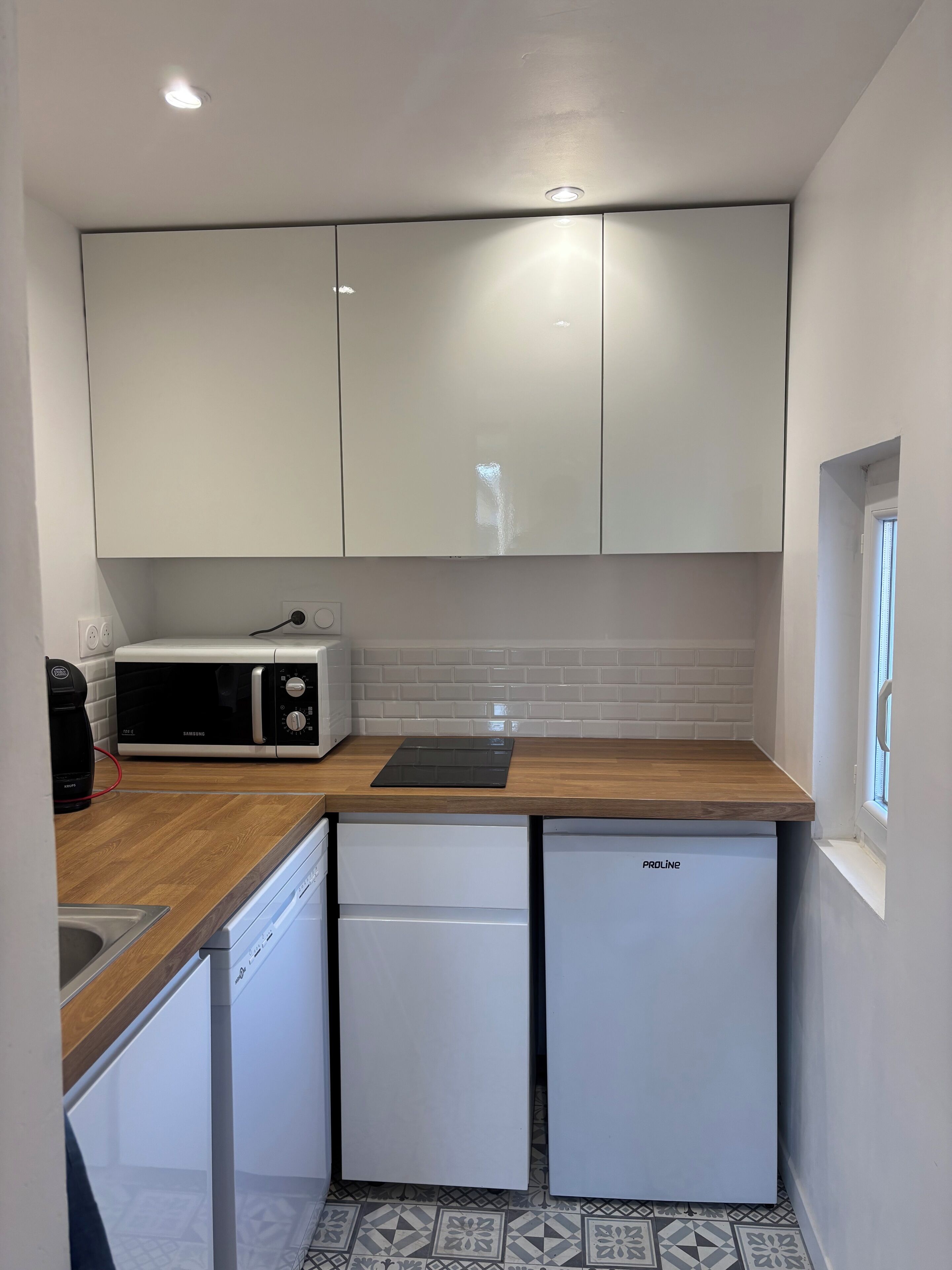 A compact kitchen with white cabinets, a microwave, a coffee maker, and a dishwasher.