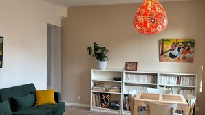 Ein Wohnzimmer mit einem grünen Sofa, einem Holztisch, einem Esstisch mit Stühlen, einem Bücherregal und einer Pendelleuchte.