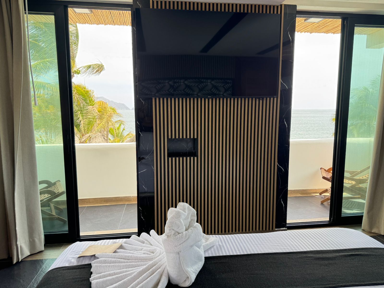 Habitación de hotel con cama, toalla, vista al mar y balcón con barandilla.