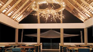 A spacious hall with a high ceiling, wooden beams, and a central chandelier. Tables and chairs are arranged along the walls. - Hotel El Mejor (San Patricio Melaque)
