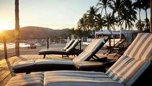 A beachside lounge area with sun loungers, a wooden deck, and palm trees in the background. - Hotel El Mejor (San Patricio Melaque)