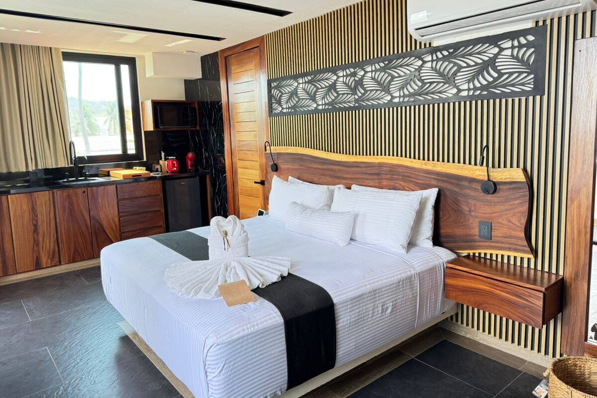 Quarto de hotel moderno com uma cama grande, cabeceira de madeira, escrivaninha embutida, micro-ondas e uma janela ampla.