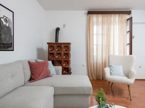 A living room with a sofa, a chair, a wooden cabinet, and a window with curtains. - Villas Casa Bianca & Maria Residence (Marcana)