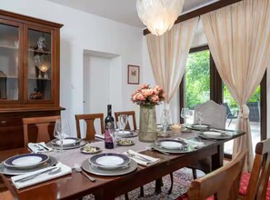 A dining room with a wooden table set for four, a cabinet with glass doors, and a vase with flowers. - Villas Casa Bianca & Maria Residence (Marcana)