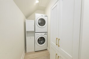 A laundry room with a stacked washer and dryer, a small shelf unit, and white cabinetry with gold handles.